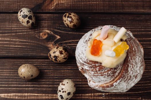 Stylish Easter cake with marshmallows and jelly bears on a dark rustic wooden background, quail eggs lie nearby. Seasonal Greetings Happy Easter. place for text. Selective focus. Top view.