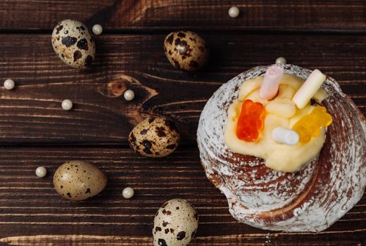 Stylish Easter cake with marshmallows and jelly bears on a dark rustic wooden background, quail eggs lie nearby. Seasonal Greetings Happy Easter. place for text. Selective focus. Top view.