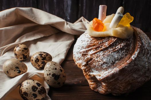 Stylish Easter cake with marshmallows and jelly bears on a dark rustic wooden background, next to it are quail eggs on a linen tablecloth, Seasonal greetings for Easter.