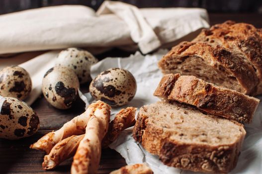 set dark yeast free buckwheat bread in a cut lies on parchment, next to quail eggs and Italian grissini. The concept of preparing breakfast.
