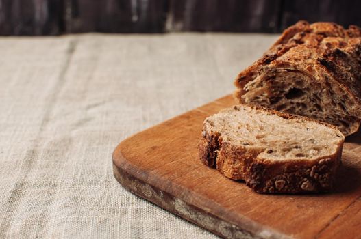 dark yeast-free buckwheat bread in a cut lies on a cutting wooden board on a wooden table covered with a linen tablecloth in a rustic style. Breakfast cooking concept.