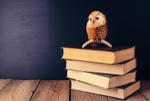 books stacked on a wooden table in a rustic style on the background a school blackboard. Owl on books as a source of wisdom and knowledge. Concept welcome back to school. copy space