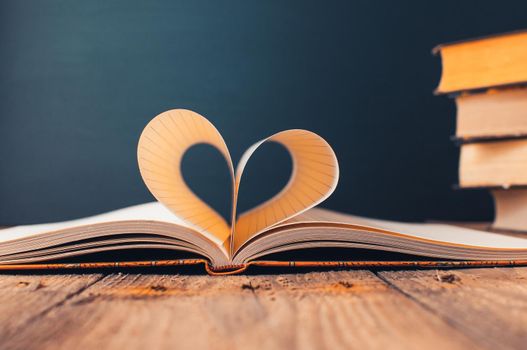 Sheets of a notebook in a cage wrapped in the shape of a heart.In the background is a stack of books and a black board.Education concept.Valentine's Day.Copy space.Rustic and vintage.Concept love.