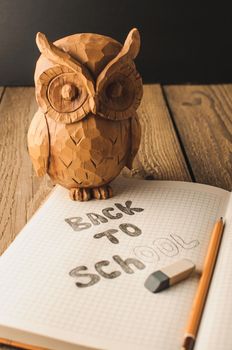 Back to school, the concept of parenting. Owl on a wooden table. The inscription on the slate color chalk. School supplies, rustic.