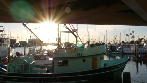 Oceanside, California USA - 26 Feb 2020: Harbor village with fisherman boats and yachts, pacific ocean coast marina, sea shore. Blue nautical vessel for fishing in port, fishery industry. Sunset light