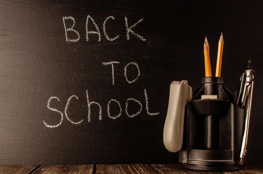 Back to school, the concept of parenting. The inscription on the blackboard with white chalk, next to it is a stand for pens with stationery. Place for text. Copy space