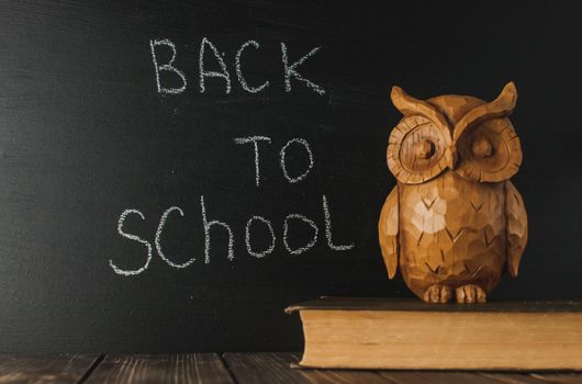 Back to school, the concept of parenting. The inscription on the blackboard with white chalk, next is the owl on the book. Place for text. Copy space.