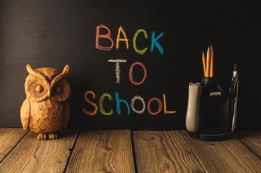 Back to school, the concept of parenting. An assortment of consumables, owl, notebook, pencils, stand for pens. The inscription on the slate black chalk. School supplies on a wooden table, rustic.