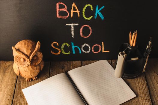 Back to school, the concept of parenting. An assortment of consumables, owl, notebook, pencils, stand for pens. The inscription on the slate black chalk. School supplies on a wooden table, rustic.
