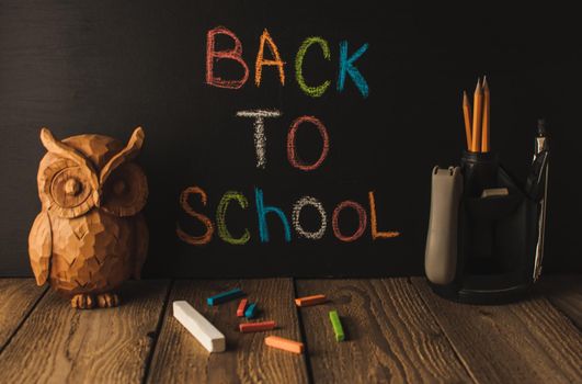 Back to school, the concept of parenting. An assortment of consumables, owl, notebook, pencils, stand for pens. The inscription on the slate black chalk. School supplies on a wooden table, rustic.