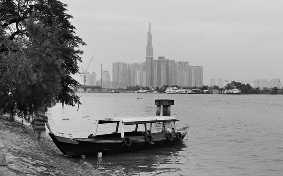 2019-11-10 / Ho Chi Minh City, Vietnam - A poor man pushes a boat into the river, with tall, modern skyscrapers in the background.
