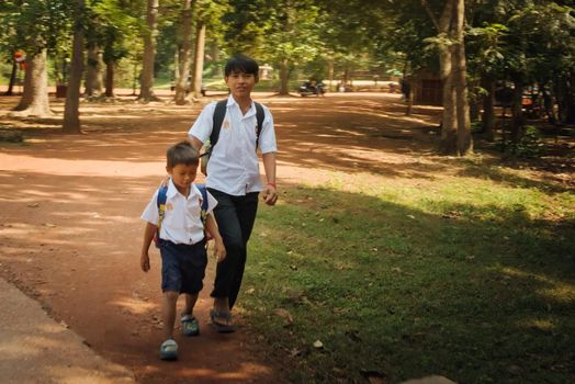 2019-11-15 / Siem Reap, Cambodia - Two boys in school uniform walk down a dirt road in a rural area.