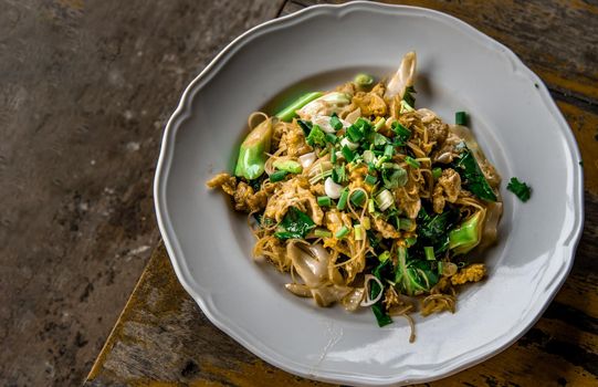 Stir-fried Noodles in Sweet Soy Sauce with Pork ( Pad See-Ew ) served in white dish on wooden table, Thai Style food, Top view, Selective focus.