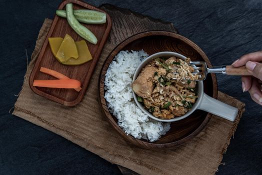 Thai food, The hand is using a fork to scoop Stir fried egg tofu with spring onion with Herbs vegetables served with steamed rice in wooden bowl.
