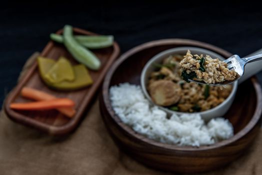 Thai food, The hand is using a fork to scoop Stir fried egg tofu with spring onion with Herbs vegetables served with steamed rice in wooden bowl.