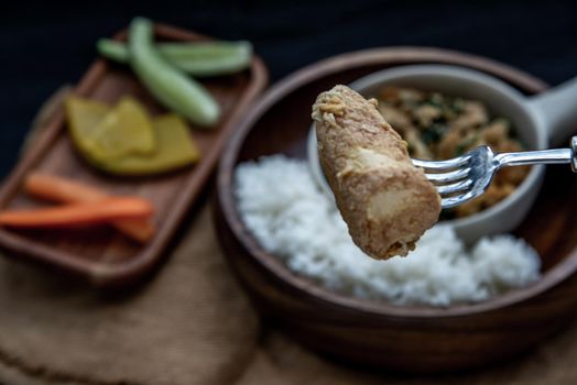 Thai food, The hand is using a fork to scoop Stir fried egg tofu with spring onion with Herbs vegetables served with steamed rice in wooden bowl.