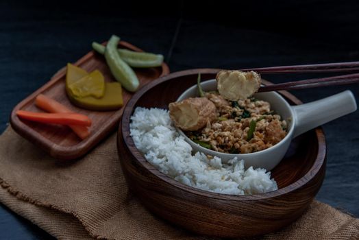 Thai food, The hand is using chopsticks to pick up  Stir fried egg tofu with spring onion with Herbs vegetables served with steamed rice in wooden bowl.