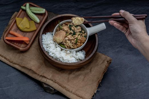 Thai food, The hand is using chopsticks to pick up  Stir fried egg tofu with spring onion with Herbs vegetables served with steamed rice in wooden bowl.