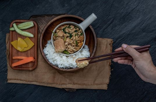 Thai food, The hand is using chopsticks to pick up  Stir fried egg tofu with spring onion with Herbs vegetables served with steamed rice in wooden bowl.