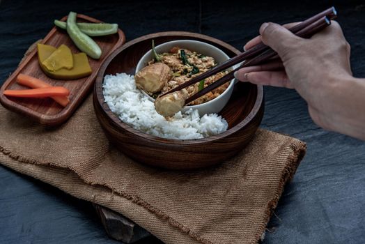 Thai food, The hand is using chopsticks to pick up  Stir fried egg tofu with spring onion with Herbs vegetables served with steamed rice in wooden bowl.