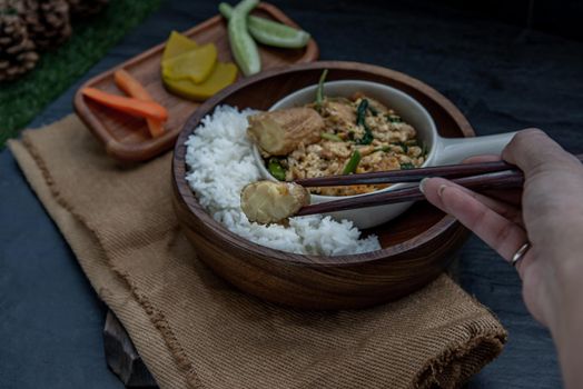 Thai food, The hand is using chopsticks to pick up  Stir fried egg tofu with spring onion with Herbs vegetables served with steamed rice in wooden bowl.