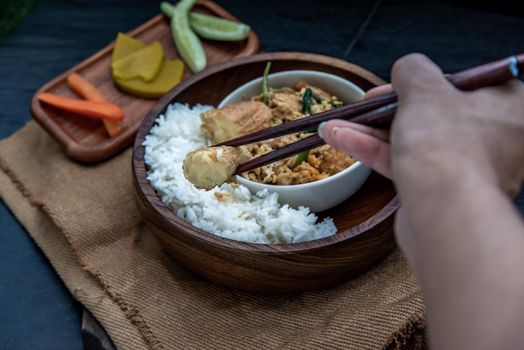 Thai food, The hand is using chopsticks to pick up  Stir fried egg tofu with spring onion with Herbs vegetables served with steamed rice in wooden bowl.