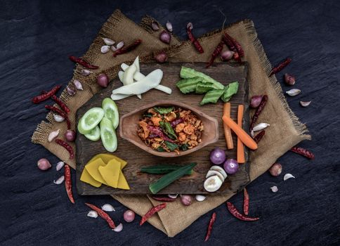 Pork Crackling Chili Paste with fried kaffir lime leaves with the ingredient and fresh vegetables on wood background, Top view.