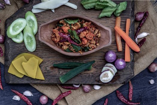 Pork Crackling Chili Paste with fried kaffir lime leaves with the ingredient and fresh vegetables on wood background, Top view.