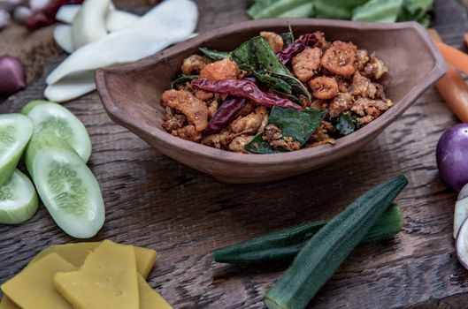 Pork Crackling Chili Paste with fried kaffir lime leaves with the ingredient and fresh vegetables on wood background, Oblique view from the top.