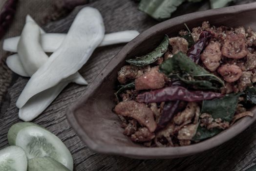 Pork Crackling Chili Paste with fried kaffir lime leaves with the ingredient and fresh vegetables on wood background, Oblique view from the top.