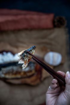 The hand is using chopsticks to pick up saba fish grilled on rice with teriyaki sauce on a sackcloth background, Japanese style.