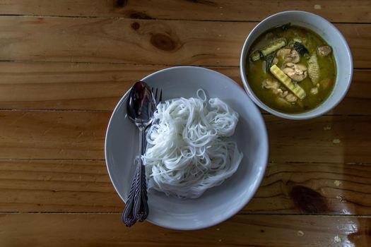 A set of Thai cuisine, spicy green curry chicken served with rice vermicelli on wooden table, very famous thai cuisine, view from above, Selective focus.