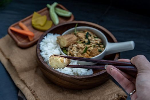 Thai food, The hand is using chopsticks to pick up  Stir fried egg tofu with spring onion with Herbs vegetables served with steamed rice in wooden bowl.