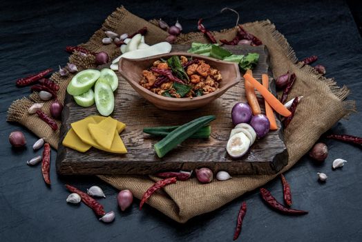 Pork Crackling Chili Paste with fried kaffir lime leaves with the ingredient and fresh vegetables on wood background, Oblique view from the top.
