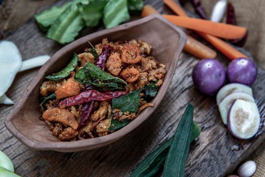 Pork Crackling Chili Paste with fried kaffir lime leaves with the ingredient and fresh vegetables on wood background, Oblique view from the top.