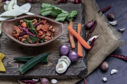 Pork Crackling Chili Paste with fried kaffir lime leaves with the ingredient and fresh vegetables on wood background, Oblique view from the top.
