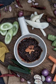 Fried chili paste with shrimps (thai language nam prik pao) with the ingredient and fresh vegetables on wood background, view from above.