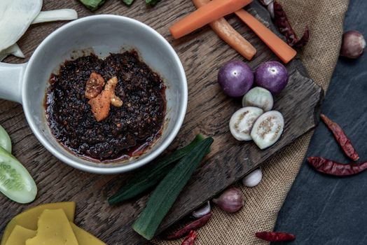Fried chili paste with shrimps (thai language nam prik pao) with the ingredient and fresh vegetables on wood background, view from above.