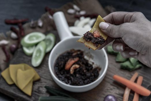 The hand is using pumpkin to scoop fried chili paste with shrimps (thai language nam prik pao) with the ingredient and fresh vegetables on wood background. Thai food.