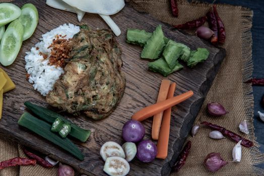 A local Thai food style, Fried acacia pennata omelet or cha-om eggs on jasmine rice with the ingredient and fresh vegetables on a wooden background, Thai Cuisine, View from above.