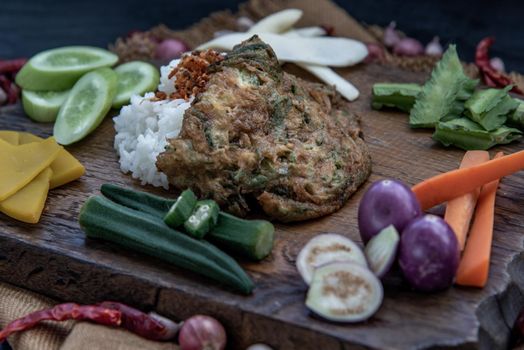A local Thai food style, Fried acacia pennata omelet or cha-om eggs on jasmine rice with the ingredient and fresh vegetables on a wooden background, Thai Cuisine, Oblique view from the top.