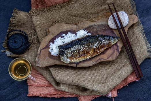 Japanese meal for dinner saba fish grilled on rice with teriyaki sauce on a wooden background served with hot tea. Japanese style, view from above.