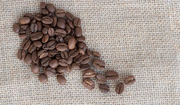 Coffee beans lie against a background of burlap. Space for text.