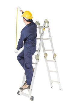 Young handyman in uniform standing on ladder while using tape measure on white, Cutout isolated on white background