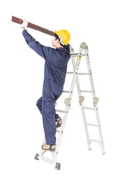 Young handyman in uniform standing on ladder construction holding wood plank on white, Cutout isolated on white background