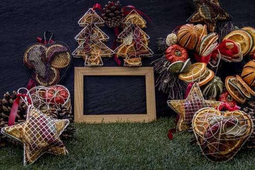 Christmas decoration, Brown natural pine cones and variety of fruits with Empty wooden frame for work about design element on lawn and dark background, Copy Space.