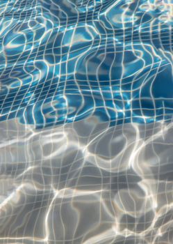 Sun reflection on the blue clear water ripples of swimming pool with mosaic bottom from above. Blue and bright water surface. Copy space, No focus, specifically
