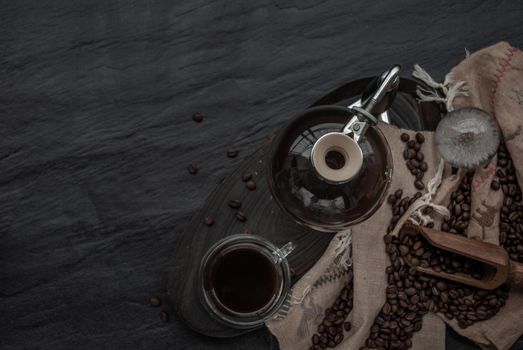 Coffee style, Cup of coffee and coffee beans roating with old wooden scoop and coffee beans around on the wooden and dark stone background. Top view with copy space for your text.