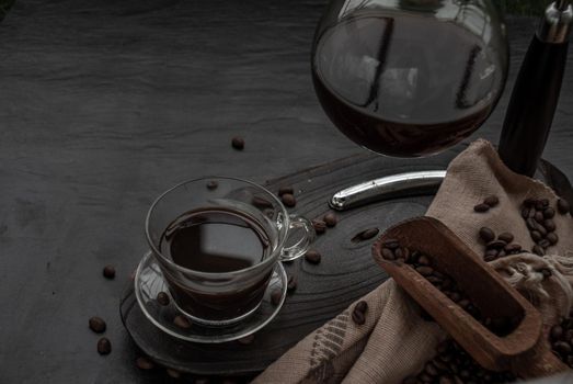 Coffee style, Cup of coffee and coffee beans roating with old wooden scoop and coffee beans around on the wooden and dark stone background. Oblique view from the top with copy space for your text.