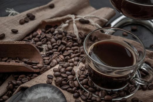 Coffee style, Cup of coffee and coffee beans roating with old wooden scoop and coffee beans around on the wooden and dark stone background. Close-up.